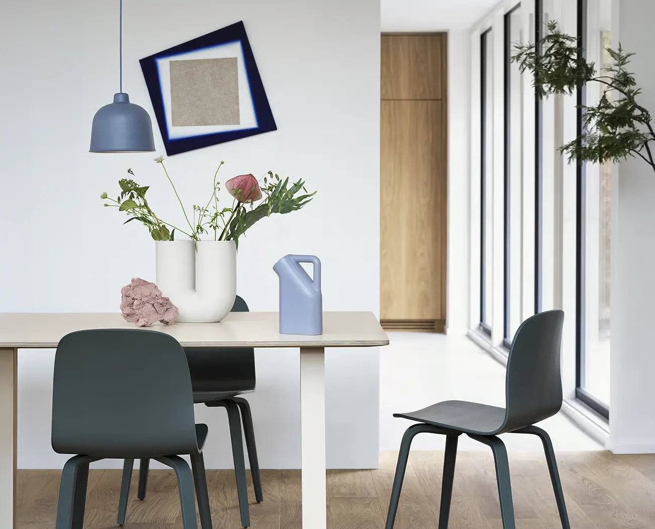 Muuto Kink Vase, 26 cm, in Cremeweiß auf einem Esstisch mit Wildblumenstrauß, im Hintergrund eine blaue Pendelleuchte
